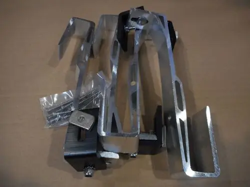 Aluminiumteile und Schrauben von Remeha, möglicherweise als Dachanker verwendet, liegen auf brauner Kartonoberfläche. Vier Hauptkomponenten sind zu erkennen.